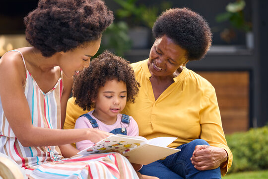 Smiling Multi-Generation Female Family Reading Book In Garden Together