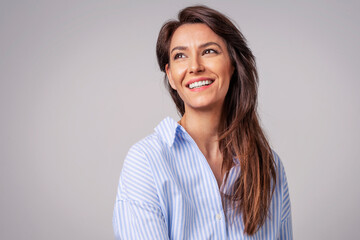 Studio portrait of attractive woman wearing shirt and laughing while sitting at isolated grey...