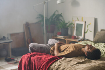 Young man lying on bed in his bedroom among smoke in depressed state