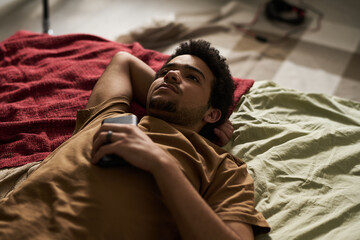 High angle view of guy lying on bed with smartphone and thinking about something