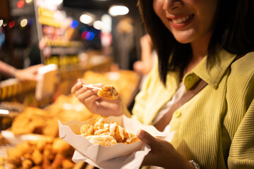 Asian woman enjoy eating fries street food at night market. Traveler Asian blogger women Happy...