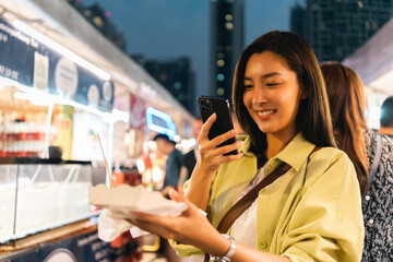 Asian woman enjoy eating fries street food at night market. Traveler Asian blogger women Happy tourists Beautiful female with Traditional thailand bangkok food.