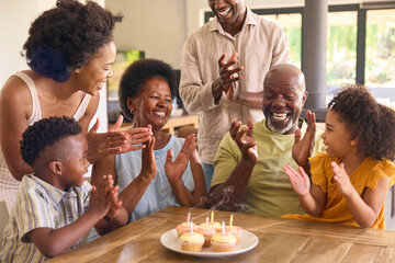 Multi-Generation Family Celebrate Grandmother's Birthday With Cake And Candles Around Table At Home 