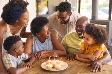 Multi-Generation Family Celebrate Grandmother's Birthday With Cake And Candles Around Table At Home 