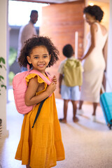 Portrait Of Girl By Door With Backpack As Family Leave Home For Holiday Or Vacation