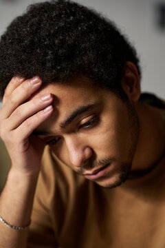 Vertical image of young guy holding his head sitting alone in his problems