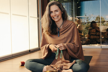 Mature woman meditating with a beads necklace at home