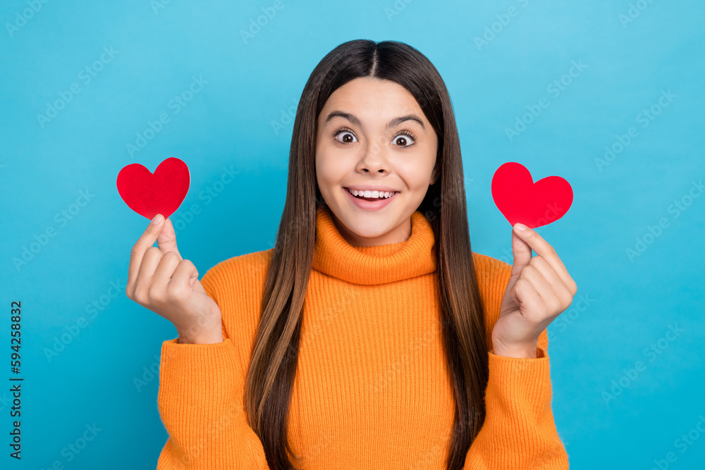 Sticker Photo of cheerful funky girl with long hairstyle wear knit turtleneck hold two paper hearts staring isolated on blue color background