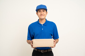Happy delivery asian man in blue uniform standing holding box parcel cardboard on isolated white background. Smiling male service worker. Delivery courier and shipping service.