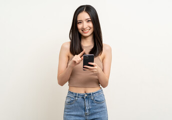 Pretty young asian woman using smartphone standing on isolated white background. Excited Beautiful...