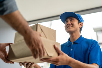 Asian delivery man with parcel in hand of blue uniform sending parcel to customer front of the house from shopping online with good service. Courier man send a package to destination.