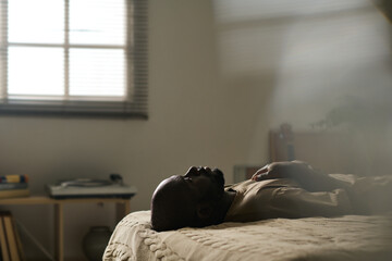 African American man in melancholy lying on bed alone in his bedroom