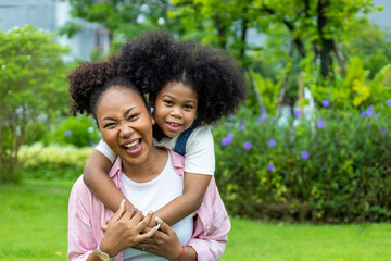 African American mother is playing piggyback riding and hugging with her young daughter while...