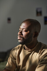 Vertical image of African American man sitting with his eyes closed and meditating at home
