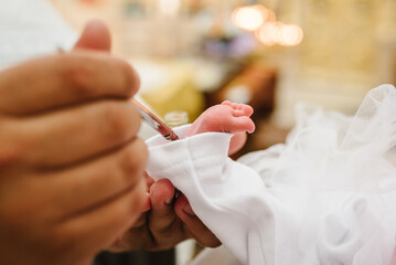 Baptism ceremony of a baby. Close up of tiny baby feet, the sacrament of baptism. The godfather holds the child in his arms. Priest and godmother hold child's legs. Temple, Orthodoxy.