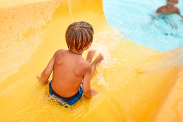 Joyful boy descends from the water slide in the water park, children's attractions in the water...