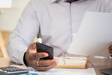 African black businessmen sit on mobile phones communicating with clients and making financial reports and studying annual profit analysis. An accountant checks the financial status of the company.