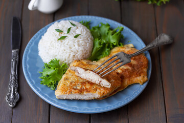 Sliced Chicken Schnitzel or chicken chop fried in sour cream batter served on a plate with green salad and cooked white rice. Selective focus, horizontal, dark wooden background.
