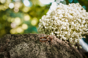 Two golden wedding rings on a stone, a bouquet of white flowers of the bride in the background