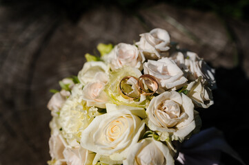 Two golden wedding rings on a stump, a bride's bouquet of flowers in the background