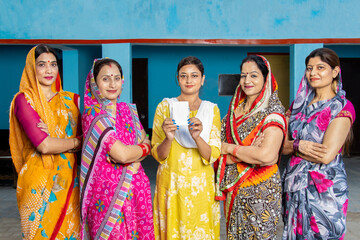 Young indian woman holding sanitary pad in hand standing with other traditional women. Spreading...