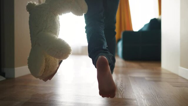 baby running indoors with bare feet. close-up of the kid leg runs with a toy bear. happy family kid concept. baby running and playing dream indoors. little girl daughter runs around fun the house