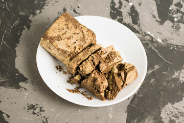 Delicious halva with cocoa on a white plate on a light gray concrete background