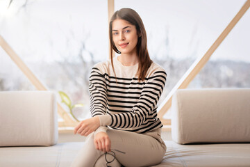 Attractive young woman looking at camera and smiling while relaxing on the sofa at home - 594279256