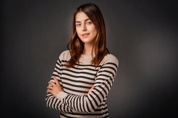 Close-up of confident young woman with folded arms against dark background - 594279666