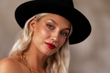 Headshot of a blond haired young woman wearing black hat and red lipstick