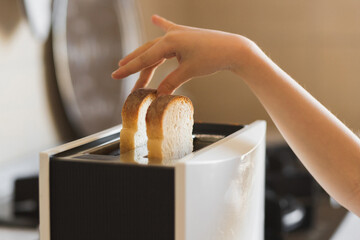 Close-up of a child's hand that inserts white slices of bread into a toaster. - obrazy, fototapety, plakaty