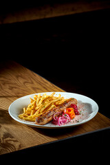 Bavarian meat sausage with a side dish of french fries, onions in a plate on a wooden background. bratwurst