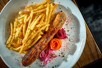 Bavarian meat sausage with a side dish of french fries, onions in a plate on a wooden background. bratwurst