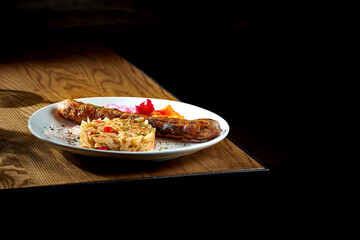 Bavarian meat sausage with a garnish of stewed sauerkraut, onions in a plate on a wooden background