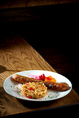 Bavarian meat sausage with a garnish of stewed sauerkraut, onions in a plate on a wooden background