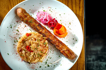 Bavarian meat sausage with a garnish of stewed sauerkraut, onions in a plate on a wooden background