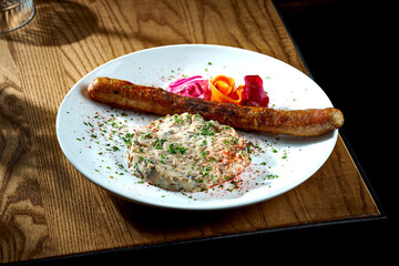 Bavarian meat sausage with a garnish of stewed mushrooms in sour cream, onions in a plate on a wooden background