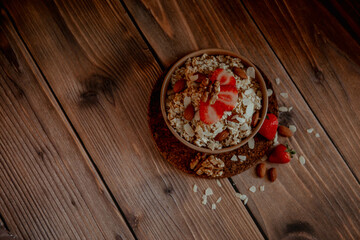Fototapeta na wymiar Oatmeal porridge with strawberries and nuts on dark wooden background
