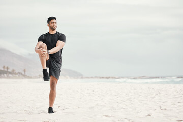 Stretch your day by starting it with a workout. a young man stretching on the beach.
