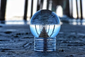 Closeup of a crystal ball reflecting surface on a beach under a fishing pier