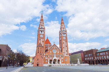 Obraz premium The beautiful Votive Church of Szeged stands as a landmark to the city history and religious heritage. Its stunning architecture towers high above the clouds.