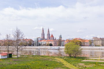 Fototapeta premium Szeged, Hungary colorful cityscape is reflected in the river Tisza below, framed by clouds and majestic architecture on a bright day.