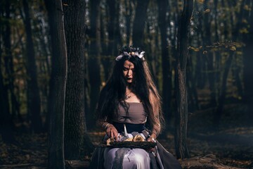 Fototapeta na wymiar Young female with long hair and face paint in a witch costume casting a spell in a forest