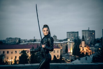 Female in black ninja assassin costume holding a sword, blurred cityscape background