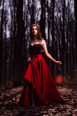Fototapeta premium Beautiful Caucasian woman in black and red dress in mysterious autumn forest with fallen dry leaves
