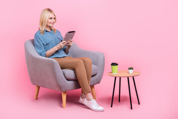 Full length photo of sweet positive lady dressed grey blouse sitting cafeteria reading news device isolated pink color background