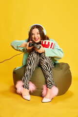 Portrait of young girl, woman in chic clothes holding popcorn and playing video games with tense...