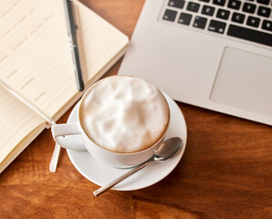 Start your day the caffeinated way. a cup of coffee on a table with a laptop.