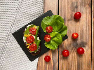 Sandwich with cherry tomatoes, lettuce, egg and cottage cheese on rye bread on a wooden background,...