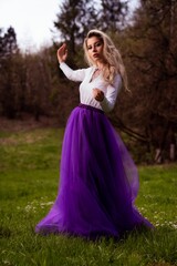 Obraz na płótnie Canvas Young female posing in a white shirt and a purple tulle skirt in a park